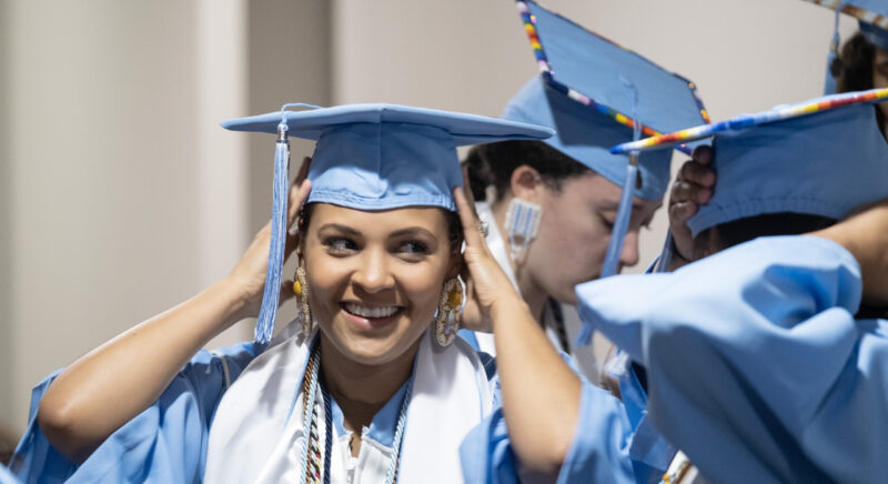Graduating student smiles placing graduation cap on their head.