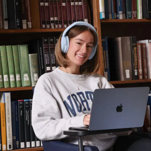 Female student wearing blue headphones looking up from her computer to smile at the camera for a picture