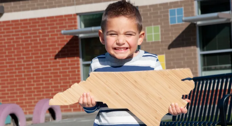 Child holding North Carolina state block.
