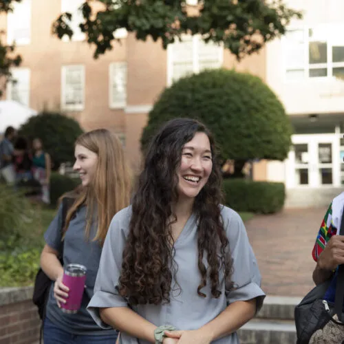 Students standing outside of the Gillings School of Global Public Health building smile while casually walking.