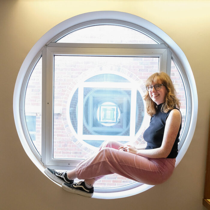 Davis Library student employee Abbey Allred sits in a circular window.
