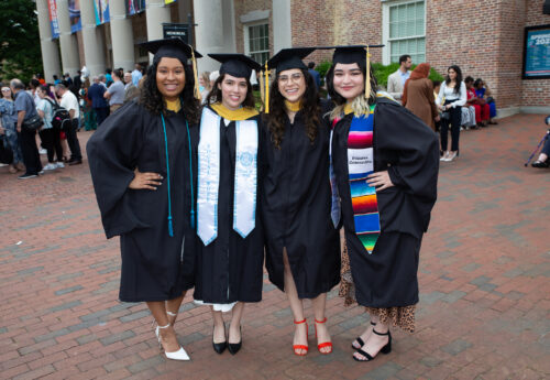 Four female School of Social Work graduates pose in their caps and gowns.