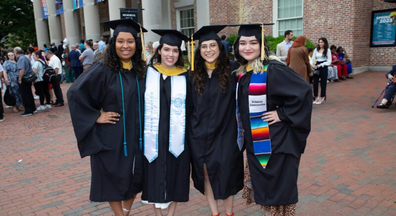 Four female School of Social Work graduates pose in their caps and gowns.