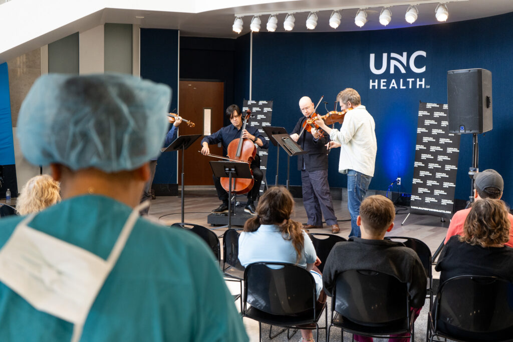 String quartet performing at UNC Health event with families and doctors in the audience.