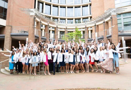 Adams School of Dentistry students wear their white coats outside of the dental school building.