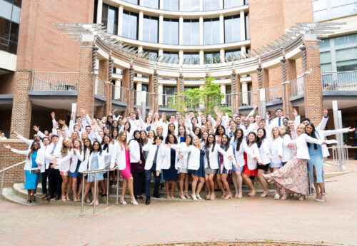 Adams School of Dentistry students wear their white coats outside of the dental school building.
