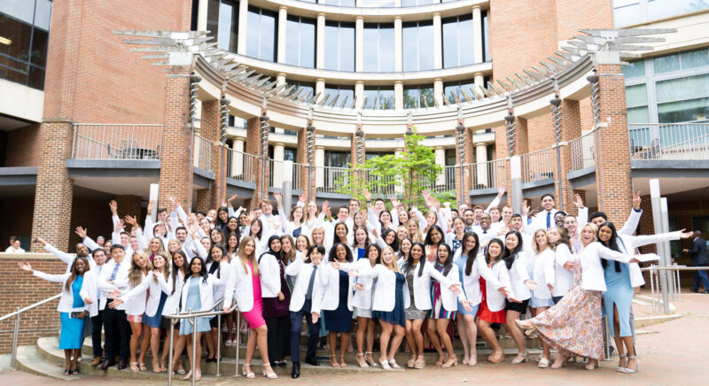 Adams School of Dentistry students wear their white coats outside of the dental school building.