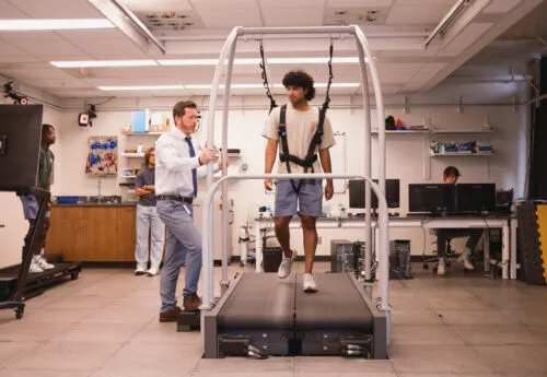 Two people in lab, one person is walking on treadmill, other person is observing