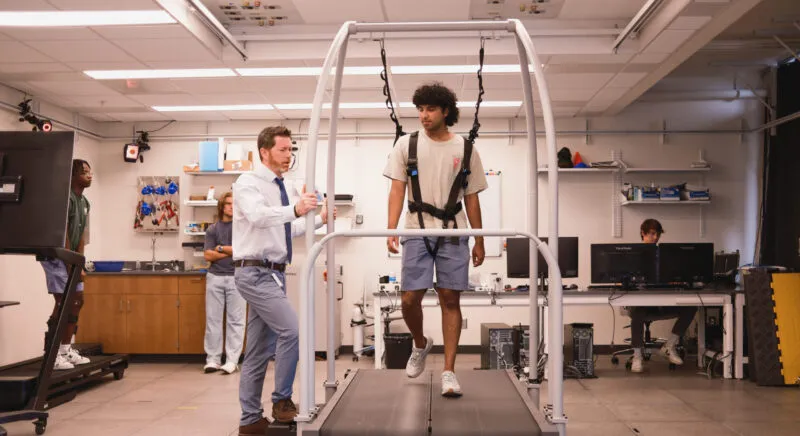 Two people in lab, one person is walking on treadmill, other person is observing