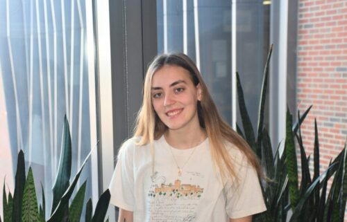 Emma Sampson ’25 poses in a white t-shirt with plants and a window behind her.