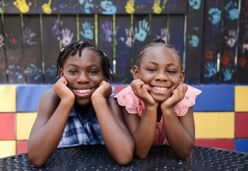 Two young girls sitting at a table smiling.