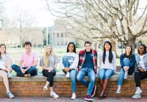 A group of UNC students sit along a low stone wall in the fall