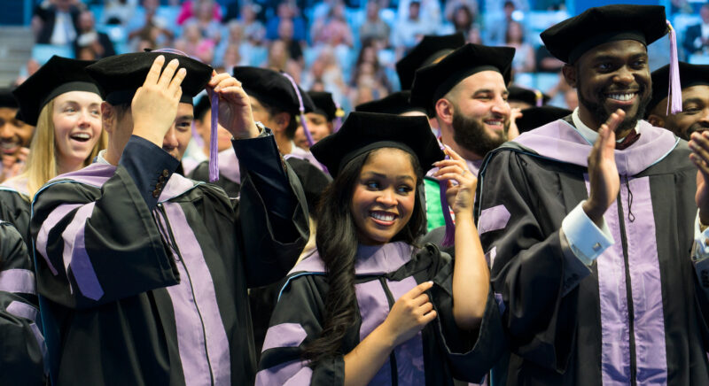 Dental graduates in graduation gowns and hats celebrating.