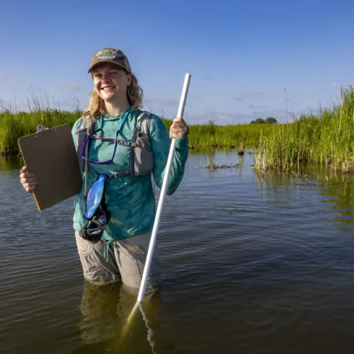 Female student wading in water with clipboard