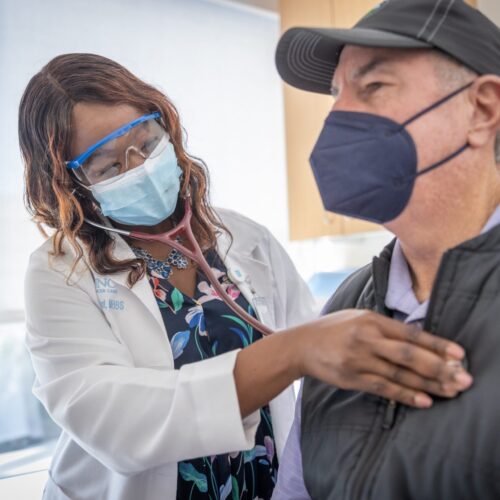 A doctor in a mask using a stethoscope to examine a patient
