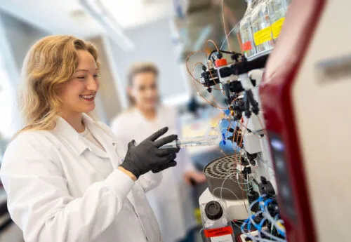 A student in a white coat uses laboratory machines