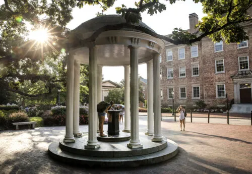 Student drinking from Old Well at UNC-Chapel Hill as the sun glows through the trees
