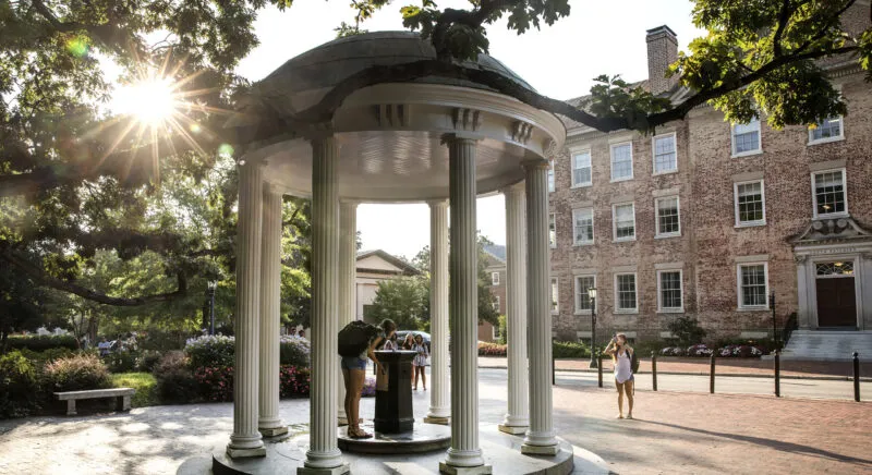 Student drinking from Old Well at UNC-Chapel Hill as the sun glows through the trees