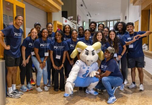 A group of students in navy t-shirts posing with Rameses.