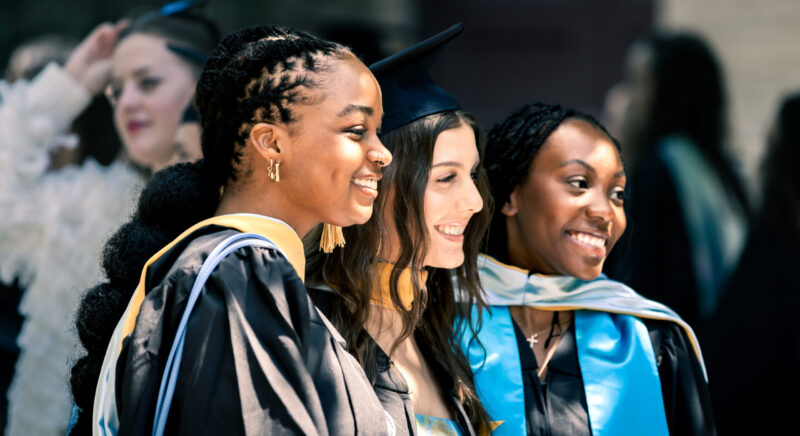 Three female School of Social Work graduates wearing regalia and looking off camera