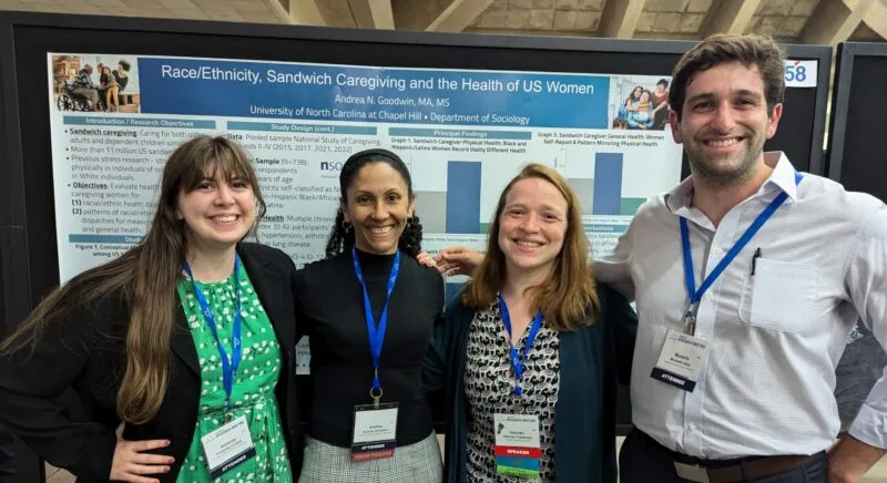 Four students posing in front of a project board