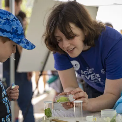 A student teaches a young kid outdoors