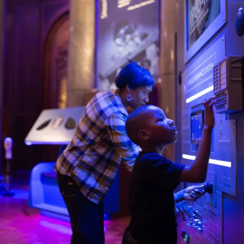 A woman and child explore a control station of the Apollo space shuttle