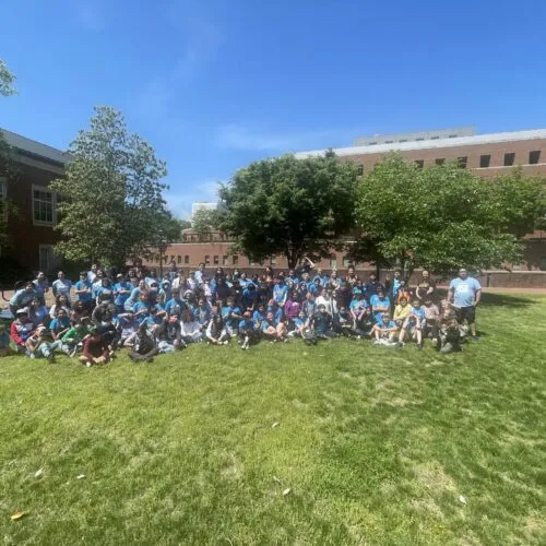 Large group of people wearing turquoise shirts posed for a photo on a lawn.