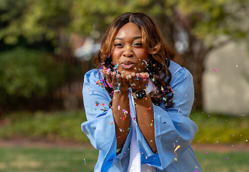 Student in graduation gown blowing confetti.