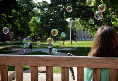 Student sitting on bench surrounded by bubbles.