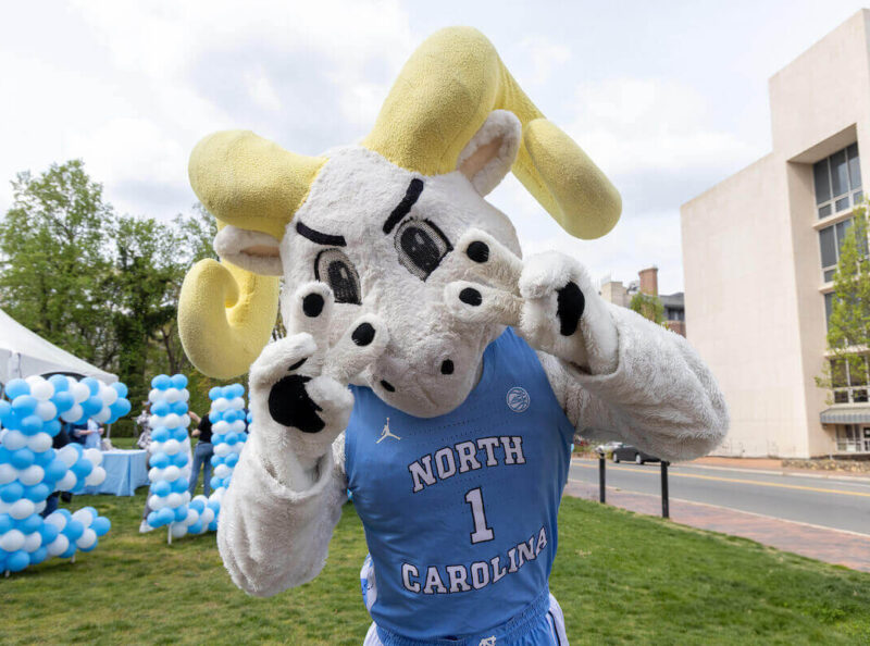 Rameses mascot showing the peace sign in front a balloon wall spelling GiveUNC