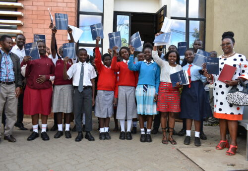 A group of students in school uniforms hold up navy blue folders that read, "Stories Across Seas."