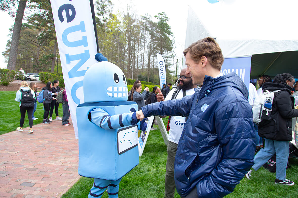 Chancellor Lee Roberts fist-bumping the Morehead robot mascot at the GiveUNC campus event